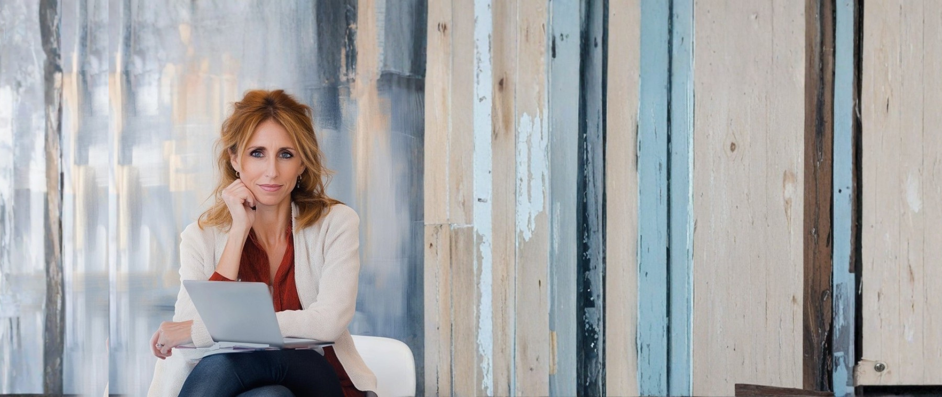 Frau mit Laptop sitzt entspannt vor einer Holz-Wand in sanften Blautönen – Symbol für Fokus, digitale Arbeit und Ruhe im Business-Alltag.